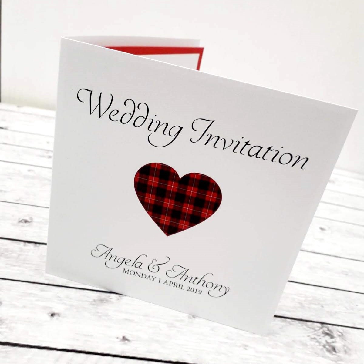 A wedding invitation with a heart showing a red and black tartan design